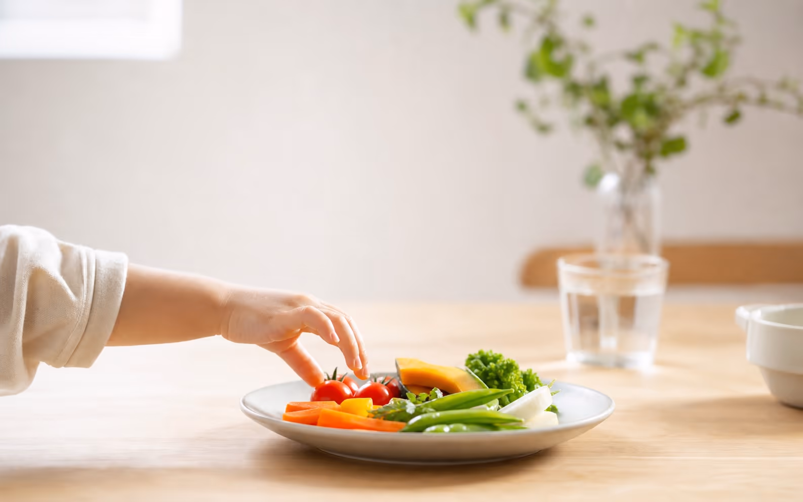 子どもの手が野菜に触れる食卓の写真